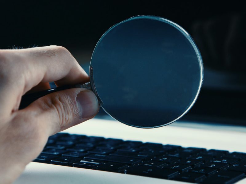 An image of a magnifying glass held next to a laptop, as the person is thinking "my insurance company is investigating me".