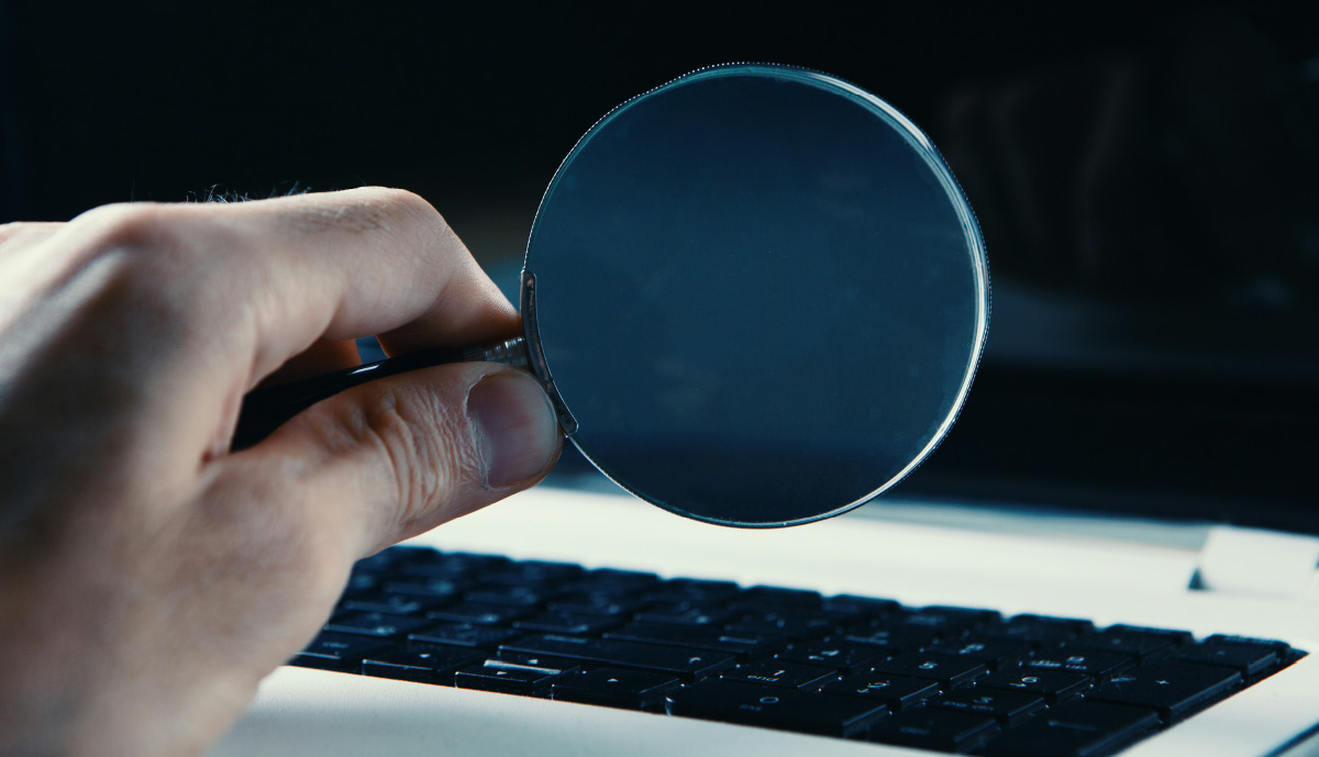 An image of a magnifying glass held next to a laptop, as the person is thinking "my insurance company is investigating me".